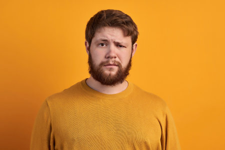 Bewildered man with thick ginger beard, raises eyebrows, reacts on fake news from friend, looks...