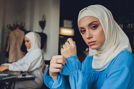 Portrait of a beautiful Asian muslim woman model wearing white blouse and blue hijab posing on white curtain as background in close-up view.の写真素材