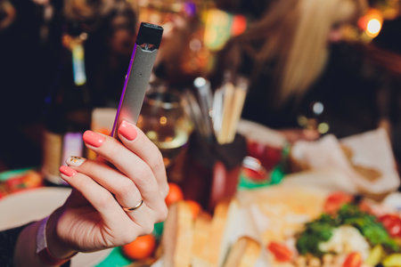 Woman smokes new Vape Pod System, inhales and exhales vapor of electronic cigarette, vaping concept.