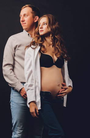 pregnant woman her husband holding her tummy.Beautiful belly of young attractive pregnant woman over black background.の写真素材