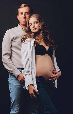 pregnant woman her husband holding her tummy.Beautiful belly of young attractive pregnant woman over black background.の写真素材