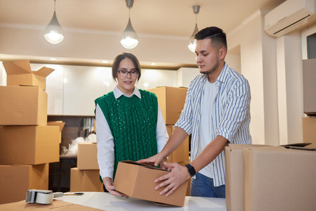Lovely newlyweds with cardboard boxes moving in new apartment, standing together on kitchen while...