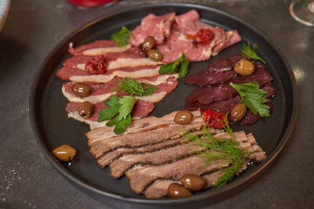 Cold smoked meat plate with prosciutto, salami, bacon, pork chops, cheese and olives on gray stone...