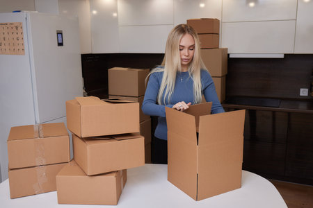 Caucasian girl taping boxes for moving in new apartment.