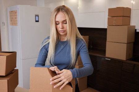Caucasian girl taping boxes for moving in new apartment.