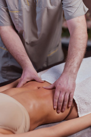 Close up of therapist doing stomach massage on woman in spa against dark background.の写真素材