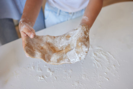 Close up image woman and little daughter knead dough with hands wooden table powdered with flour.の写真素材