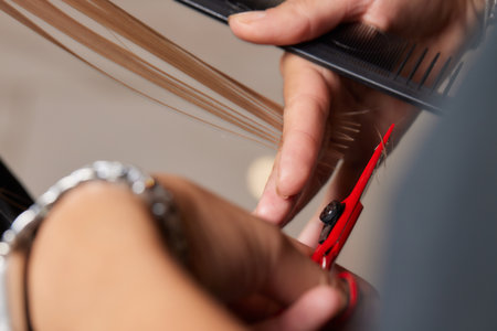 Hands of hairdresser hold hair strand between his fingers making haircut of long hair of the young woman with comb and scissors in hairdresser salon, close up.の写真素材