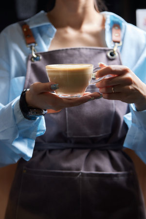 Top view shot of professional barista pouring milk from jar in to a cup of coffee, coffee being prepared by a barista. Focus on hands holding cup of coffee.の写真素材