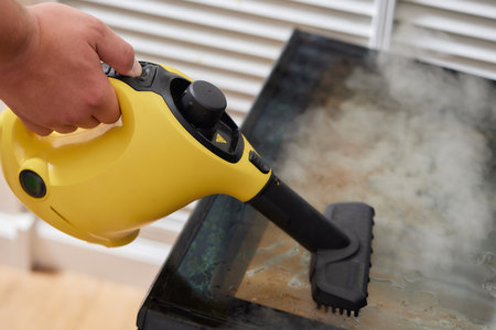 Experienced worker in rubber gloves steam-cleaning kitchen equipment.の写真素材