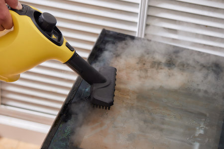 Experienced worker in rubber gloves steam-cleaning kitchen equipment.の写真素材