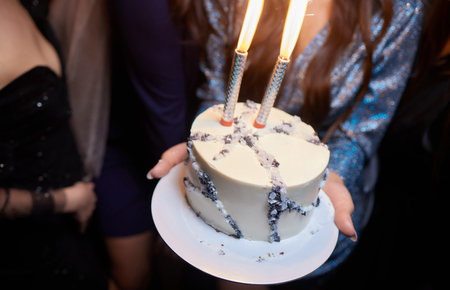 Young woman holding plate with tasty birthday cake against defocused lights.