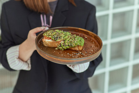 Female hand holding healthy avocado toast. ripe hass avocado, wholegrain bread, sesame flax seeds....