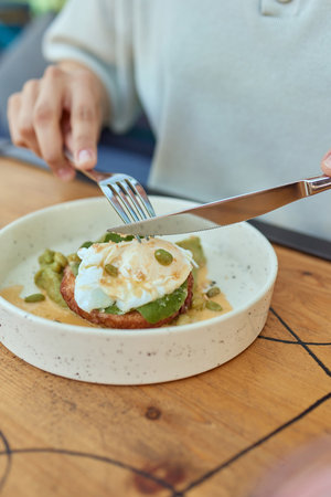 Young woman eat breakfast with knife and fork, Morning in cafe. Healthy breakfast with wholemeal bread toast with avocado, poached egg with green salad.の写真素材