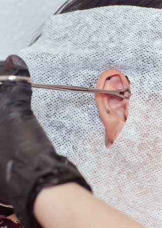piercings on an ear. Conch and helix piercings close up. Professional holding the jewel.の写真素材