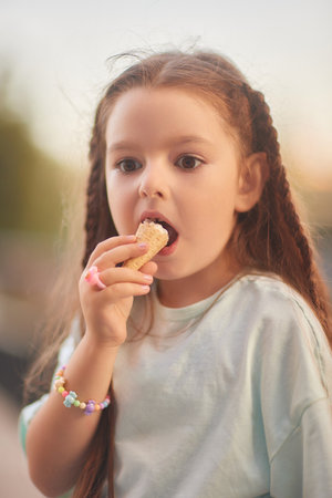 a child eats ice cream in the summer when its hot outside. Ice cream in a waffle cone. A happy and contented child in a hat and dress.の写真素材