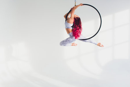 young redhead woman performs acrobatic elements in the air ring on a white background.の写真素材