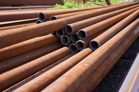 Scraps of rusty pipe of different sizes on rack in warehouse