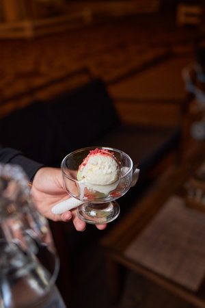 Close up of a delicious looking ice cream cup with an out of focus woman grabbing a spoonful. Shot taken from outside. Ice cream and lifestyle concept.の写真素材
