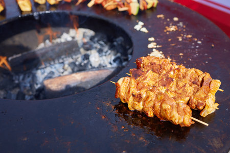 Round grill in the shape of a bowl with fire inside. A man prepares a hearth for barbecue. The round hearth is cleaned before cooking. The firewood lies in the bowl of the outdoor hearth.の写真素材