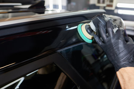 Man with an orbital polisher in car workshop polishing car closeup