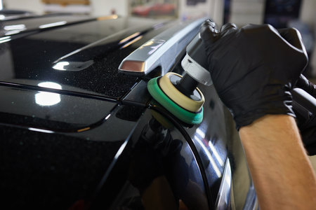 Man with an orbital polisher in car workshop polishing car closeup