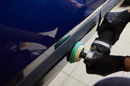 Man with an orbital polisher in car workshop polishing car closeup