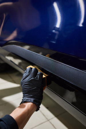 The process of applying a nano-ceramic coating on the white cars hood by a male worker in blue gloves with a sponge and chemical composition to protect the paint in detailing workshop. Auto service.の写真素材