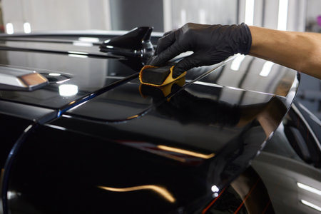 The process of applying a nano-ceramic coating on the white cars hood by a male worker in blue gloves with a sponge and chemical composition to protect the paint in detailing workshop. Auto service.の写真素材