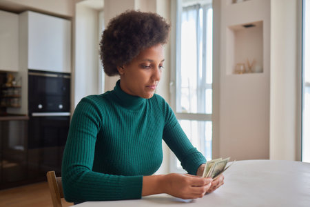 Attractive young African American woman working on finances at home wearing purple jacket sitting at dining table.の写真素材