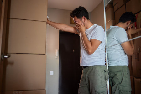 Man standing in living room on day of move to rented home, unbox carton box with belongings. Relocate to new own apartment collect personal thingsの写真素材