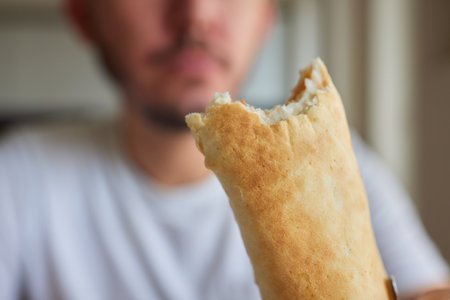 Closeup portrait of hungry man eating delicious sandwich at home on background of kitchen. Handsome...