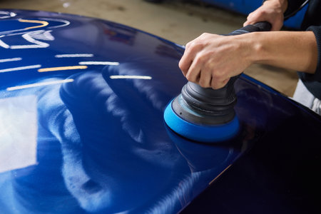 Man with an orbital polisher in car workshop polishing car closeup