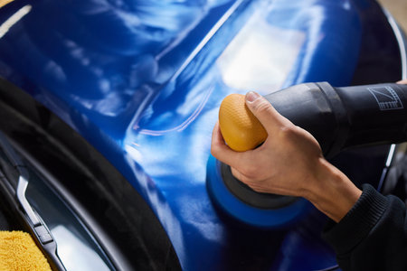 Man with an orbital polisher in car workshop polishing car closeup