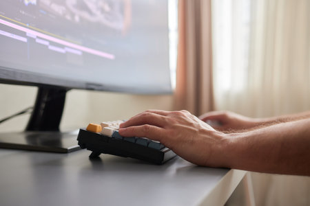 back view of young man in the dark studio color grading video with laptop and external monitorの写真素材