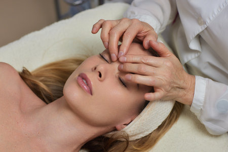 Woman receiving facial buccal massage in beauty salon.Beauty and skincare concept with a beautiful woman. Middle aged female relaxed with massage for facial liftingの写真素材
