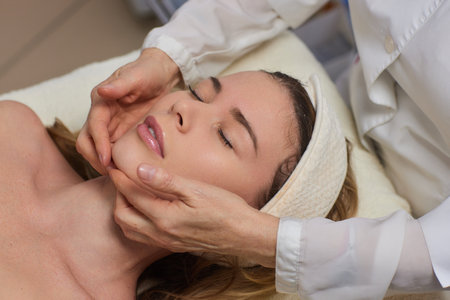 Woman receiving facial buccal massage in beauty salon.Beauty and skincare concept with a beautiful woman. Middle aged female relaxed with massage for facial liftingの写真素材