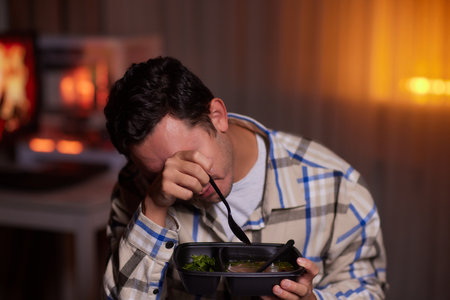 A young man in a yellow casual hoodie eats noodles with sticks and watches a movie at nightの写真素材