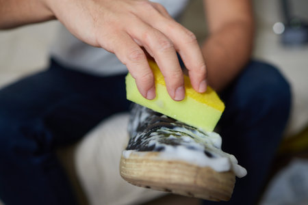 Cleaning suede sneakers. A worker in a shoe workshop cleans a pile of shoes