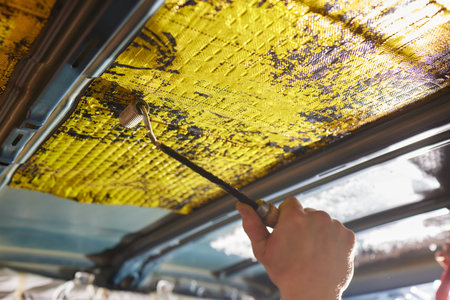 Worker glues soundproofing material to inside of car hood. Process of car sound