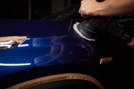 Car detailing - Man with orbital polisher in repair shop polishing car. Selective focus