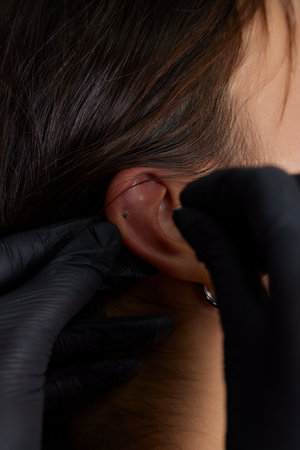 Professional placing the jewel of piercing on the temple on the head with ball. Tragus type.