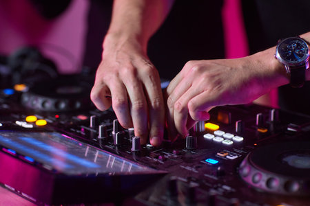 control DJ for mixing music with blurred people dancing at party in nightclub.