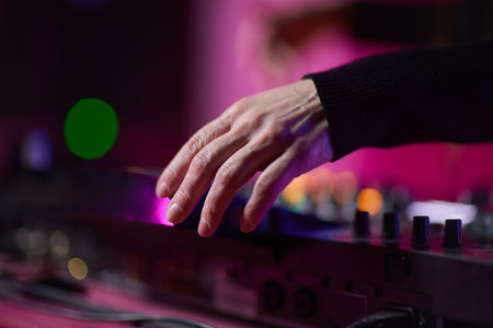 control DJ for mixing music with blurred people dancing at party in nightclub.