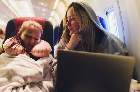 Attractive caucasian female passenger of airplane sitting in comfortable seat listening music in earphones while working at modern laptop computer with mock up area using wireless connection on board.の写真素材