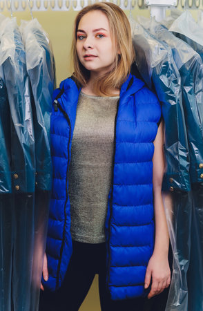 Female cleaner in laundry shop or textile dry-cleaning next to clean clothes in garment bags.の写真素材