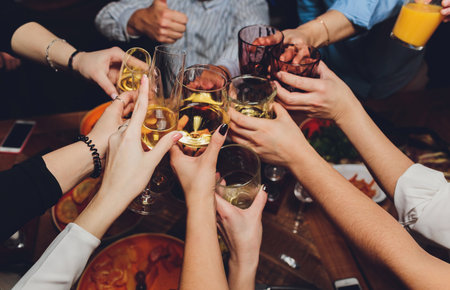 Close up shot of group of people clinking glasses with wine or champagne in front of bokeh...