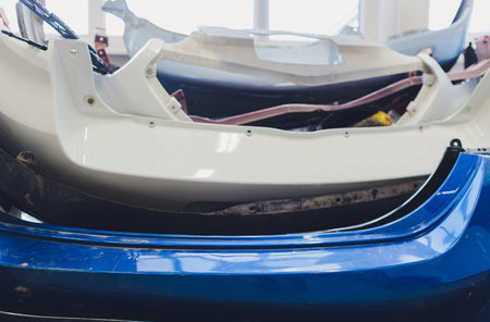 A row of car bumpers of different colors waiting their turn at a auto painters shop. They are all...