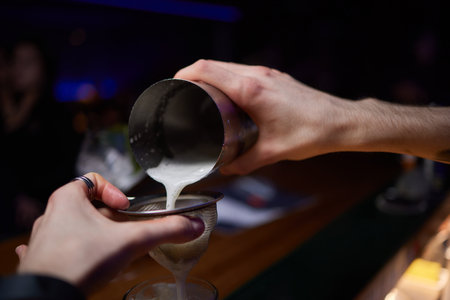 Bartender pours pink cocktail into martini glass with flairの写真素材