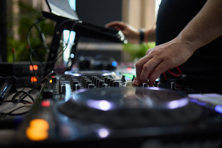 control DJ for mixing music with blurred people dancing at party in nightclub.